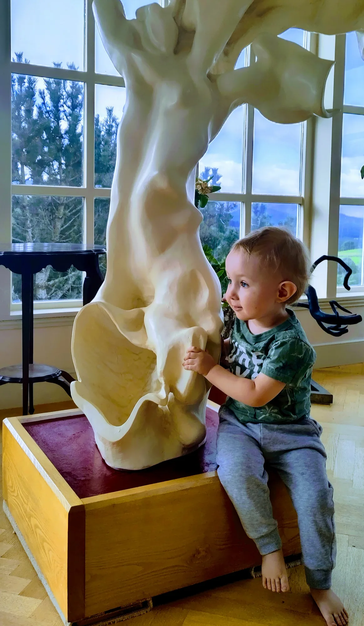 The White Hart sculpture towering over Bruce Thomson's grandson sitting at its base, showing the scale of the carved wood piece